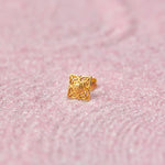 Close up of square floral inspired 18K gold nose pin placed on a soft pink textured background showcasing intricate cutwork detailing