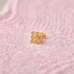 Close up of an intricate geometric design 18K gold nose pin placed on a soft pink textured background highlighting fine craftsmanship