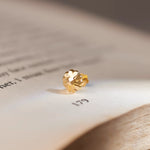 Close up of a gold nose pin placed on an open book page highlighting its polished finish and elegant detailing