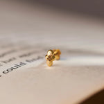 Close up of minimalist 18K gold nose pin placed on an open book page with soft natural lighting