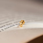 Close up view of a minimal 18K gold nose pin placed on an open book page highlighting its smooth finish and elegant form