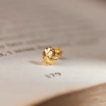 Close up of an 18K gold nose pin placed on an open book highlighting its intricate floral design and polished finish