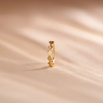 Close up of zigzag patterned 18K gold nose ring standing upright on a soft beige fabric background with natural light shadows