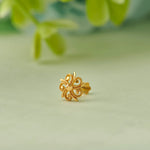 Close up of swirl inspired 18K gold nose pin placed on a soft green surface with blurred natural leaves in the background