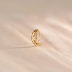 Close up of an 18K gold nose ring with delicate engraved and cutwork details, photographed upright on a soft beige textured fabric with subtle light patterns