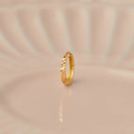 Front view of a slim textured 18K gold hoop nose ring standing upright on a soft beige background with subtle light reflections