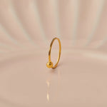 Close up of minimalist 18K gold nose ring with a small ball accent standing upright on a soft beige background with subtle light reflections