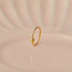 Close up of minimalist open hoop 18K gold nose ring placed on a soft beige background with gentle light reflections
