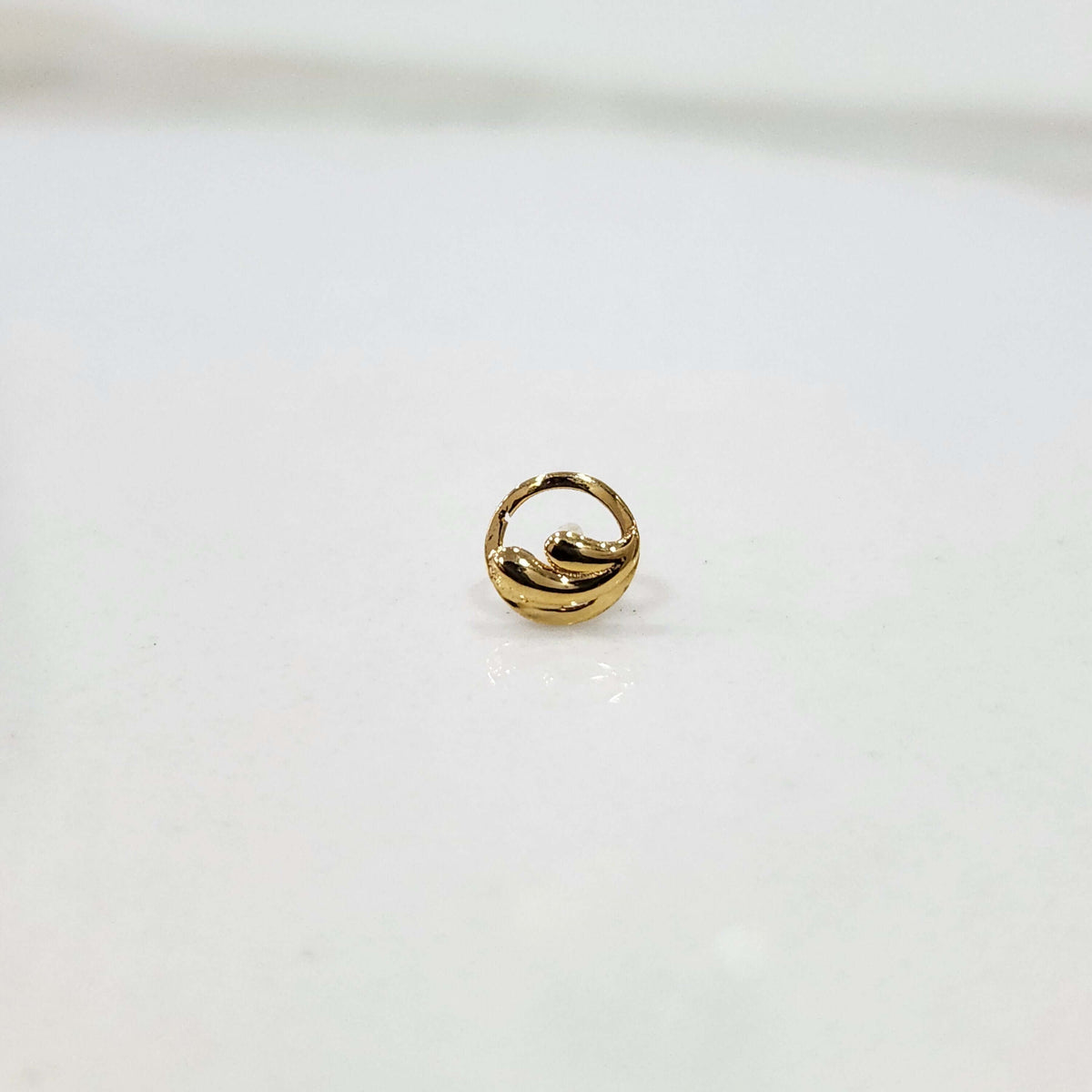 Encircled Waves gold nose pin in 18K gold displayed on plain surface showcasing elegant circular wave design