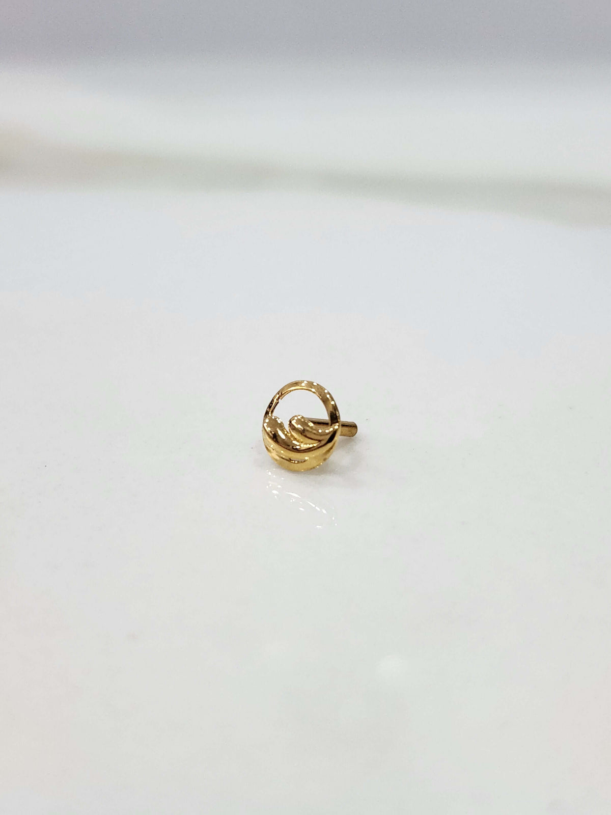 Encircled Waves gold nose pin in 18K gold displayed on a flat surface with elegant wave-inspired circular design