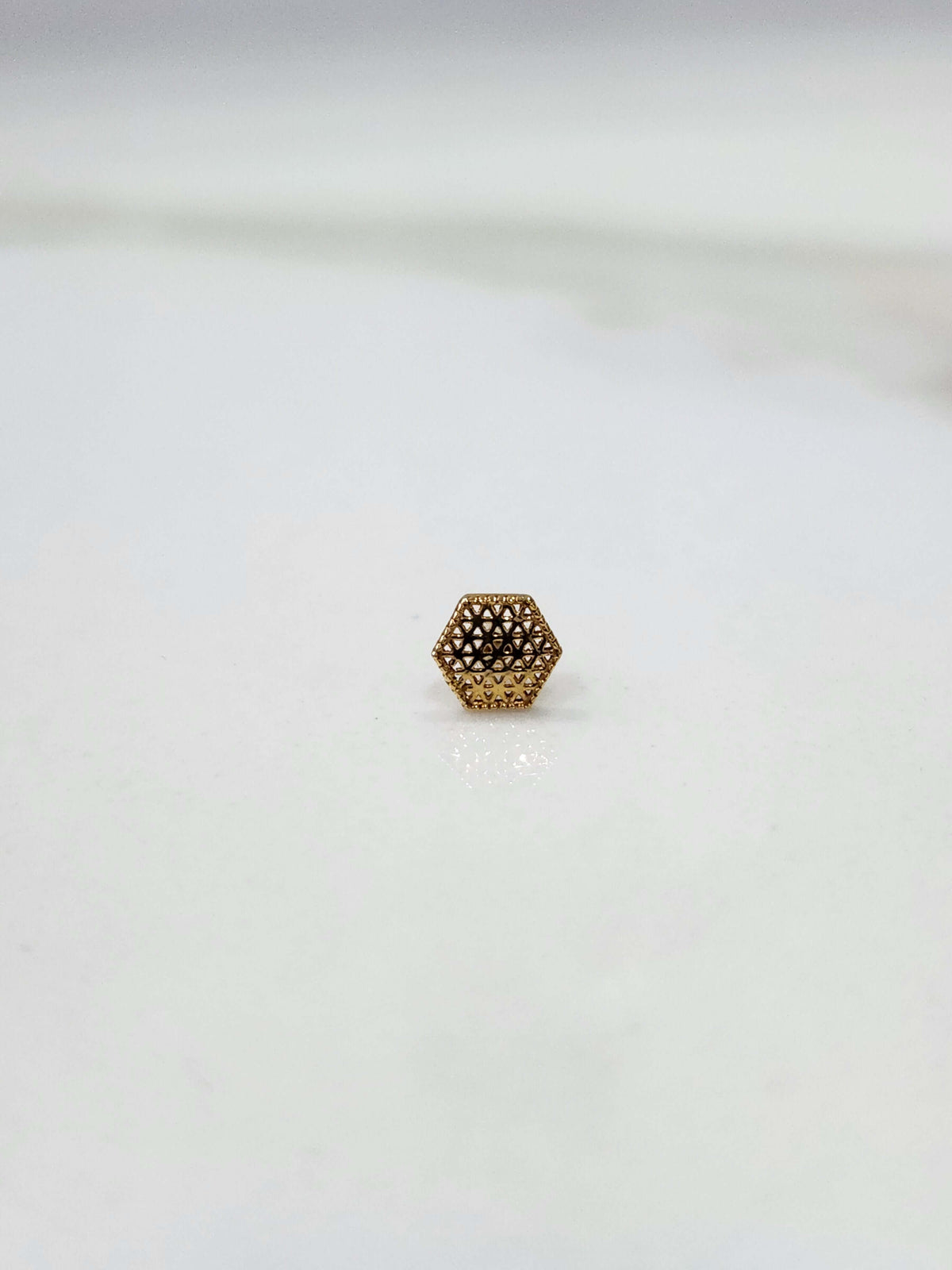 Hexa Lattice gold nose pin in 18K gold with intricate geometric hexagon lattice pattern placed on a flat surface