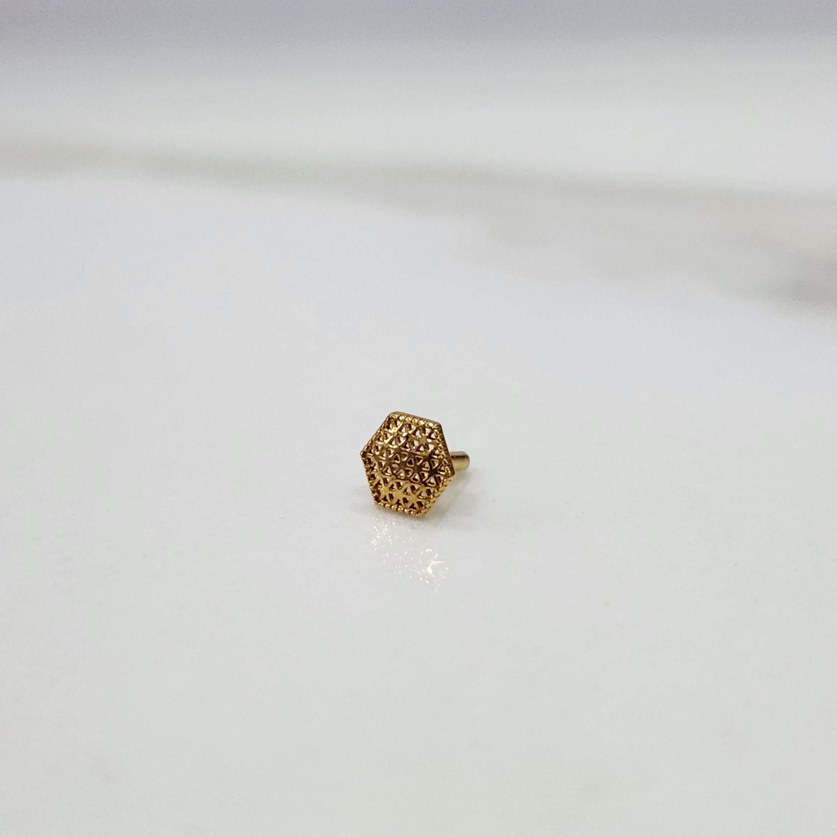Hexa Lattice gold nose pin crafted in 18K gold with detailed geometric hexagon lattice pattern, side view on flat surface