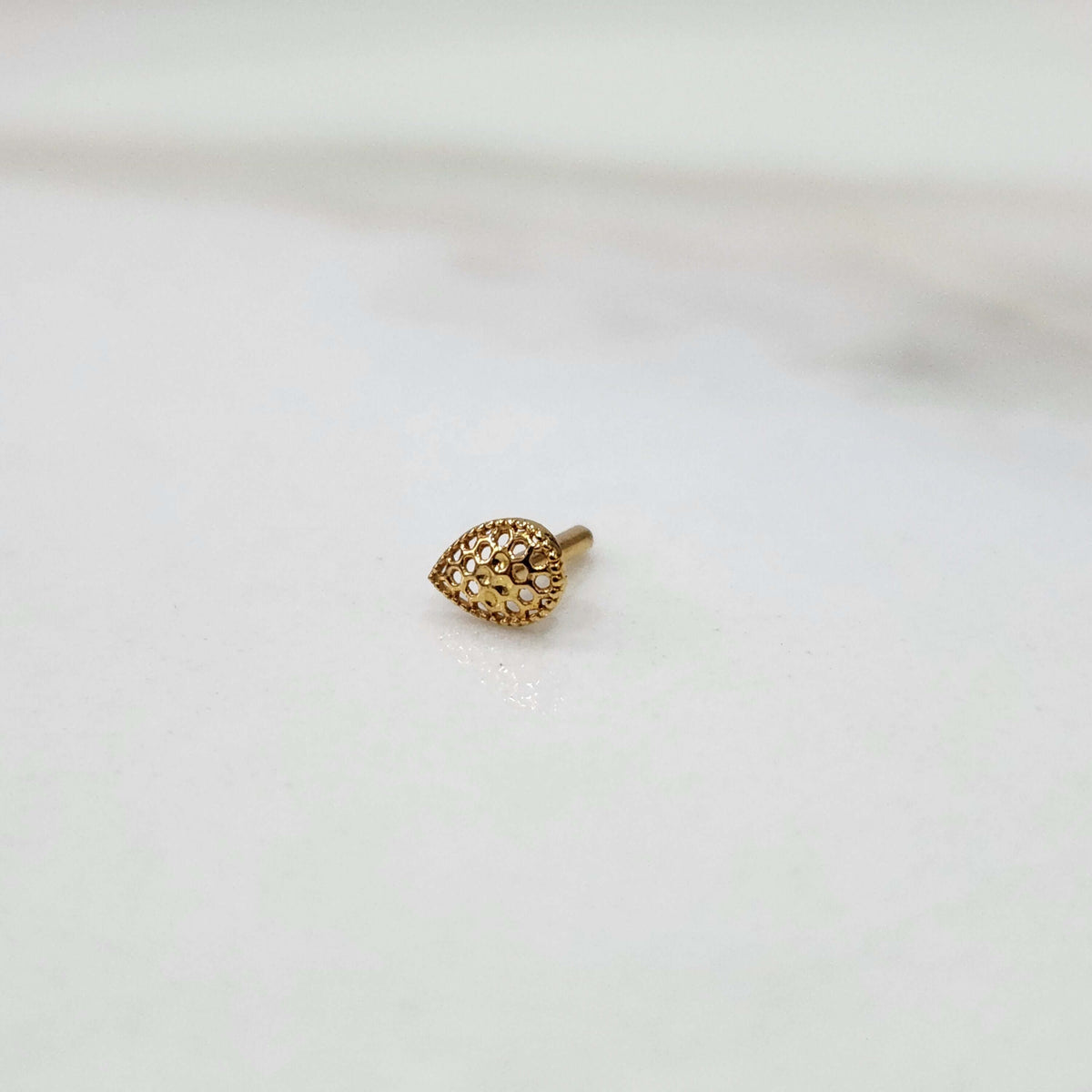 Close-up view of Honeycomb Drop gold nose pin in teardrop shape with hexagonal cutout pattern placed on white background