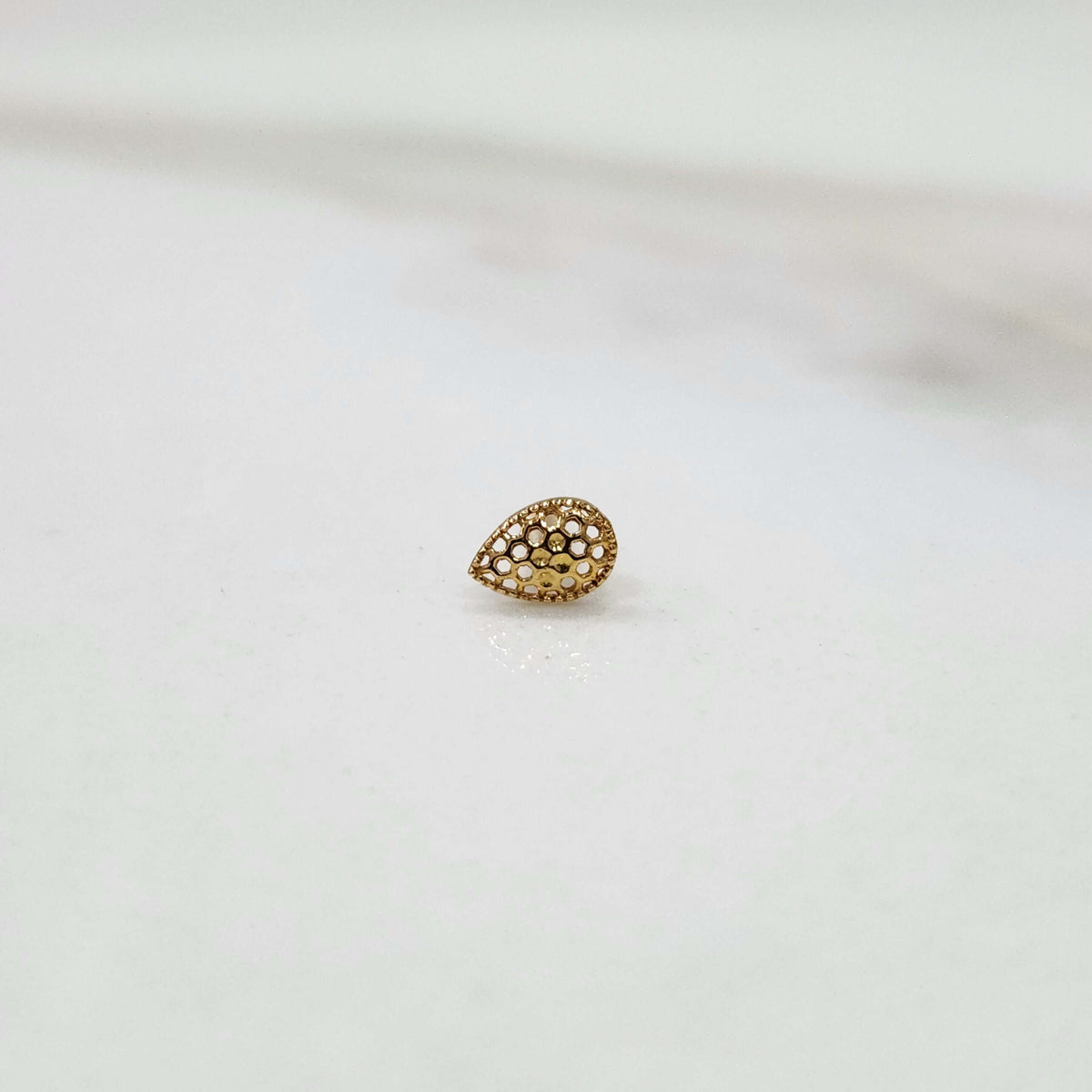 Honeycomb Drop gold nose pin in teardrop design with intricate hexagonal cutouts placed on a white surface