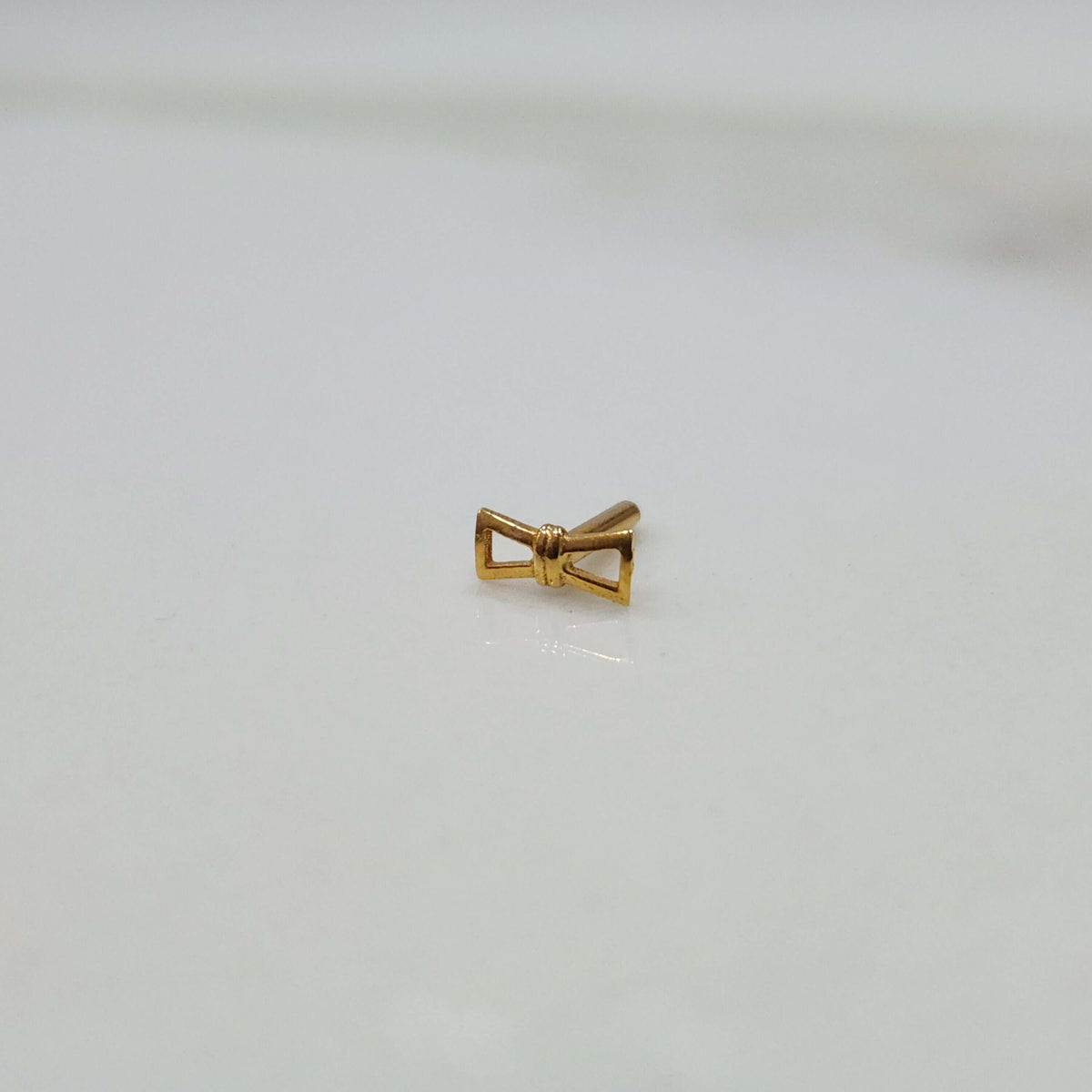 Ribbon Whisper gold nose pin with delicate bow-tie inspired design placed on a flat surface in close-up view