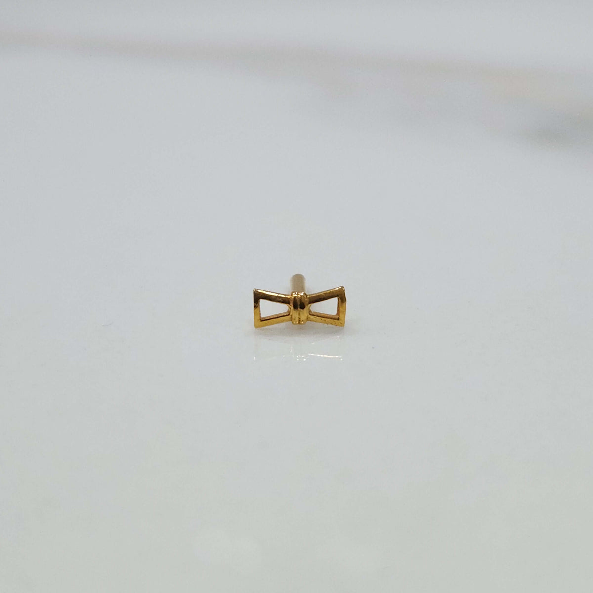 Ribbon Whisper gold nose pin featuring an elegant bow-tie inspired design placed on a flat white surface