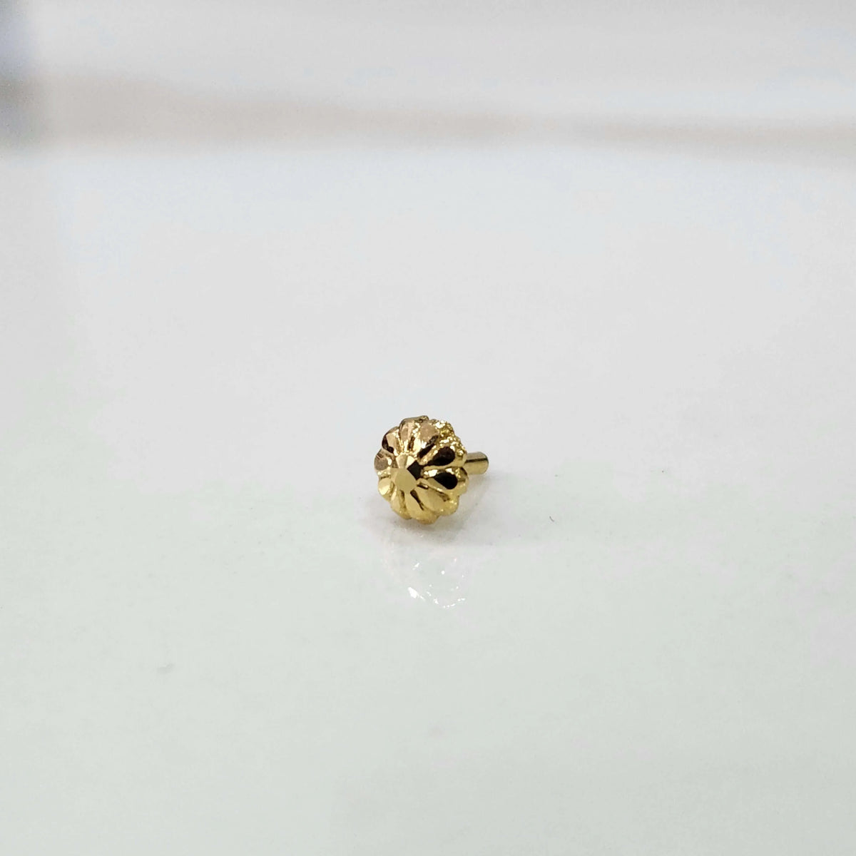 Front view of a small gold nose pin on a neutral grey background showing its compact size