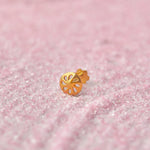 Close up of a floral cutwork gold nose pin placed on a soft pink textured surface highlighting its delicate open design