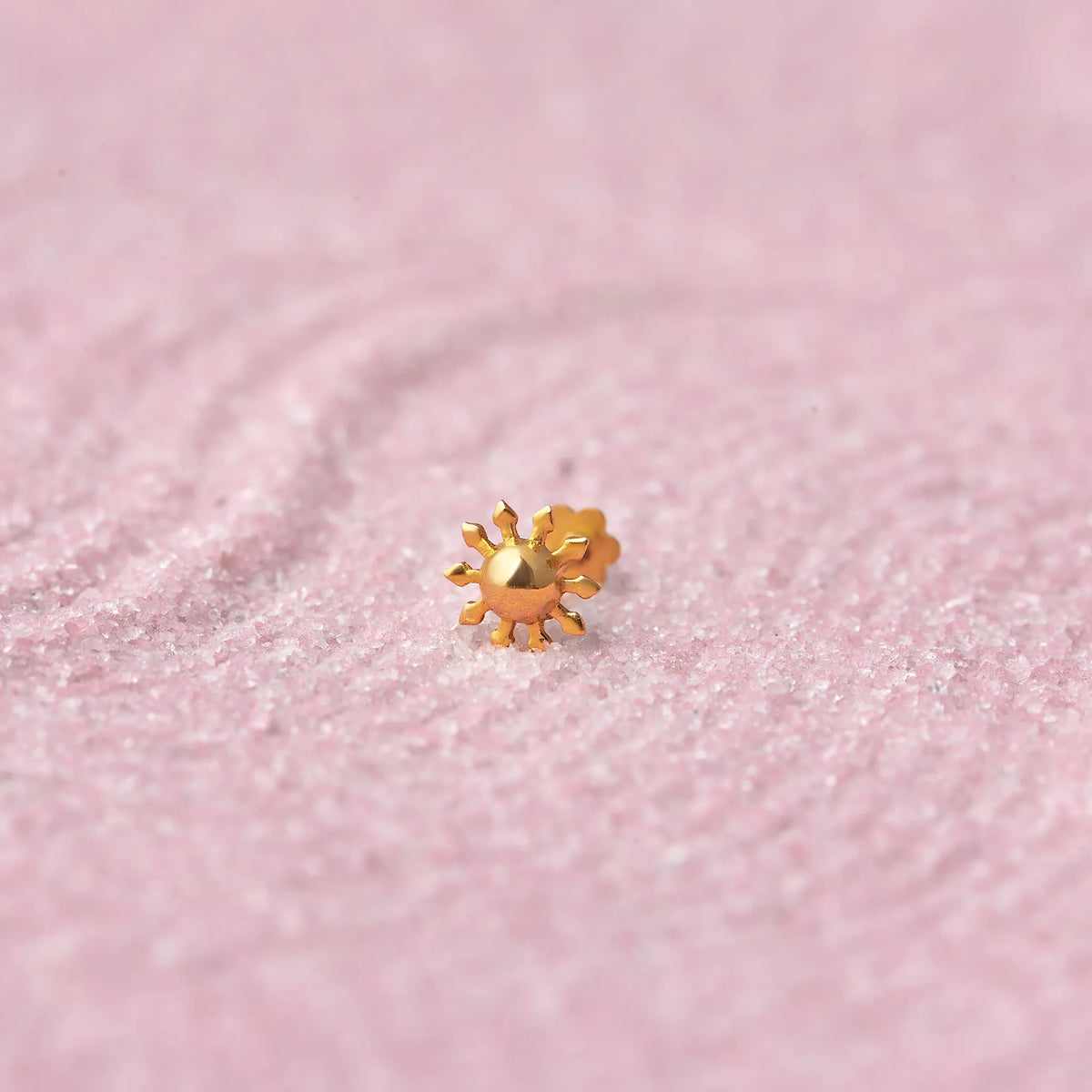 Close up of a floral design 18K gold nose pin placed on a soft pink textured background highlighting fine detailing