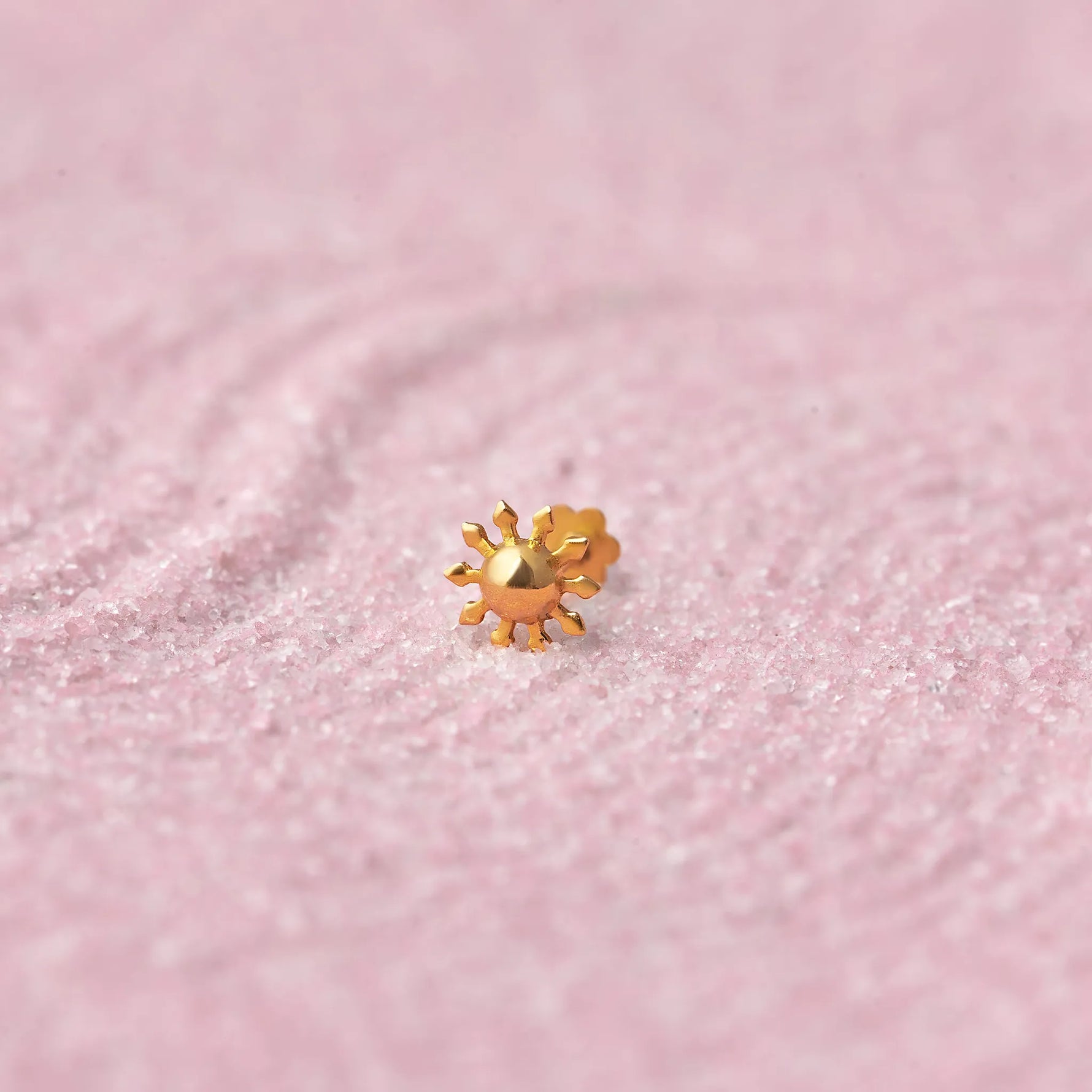 Close up of a floral design 18K gold nose pin placed on a soft pink textured background highlighting fine detailing