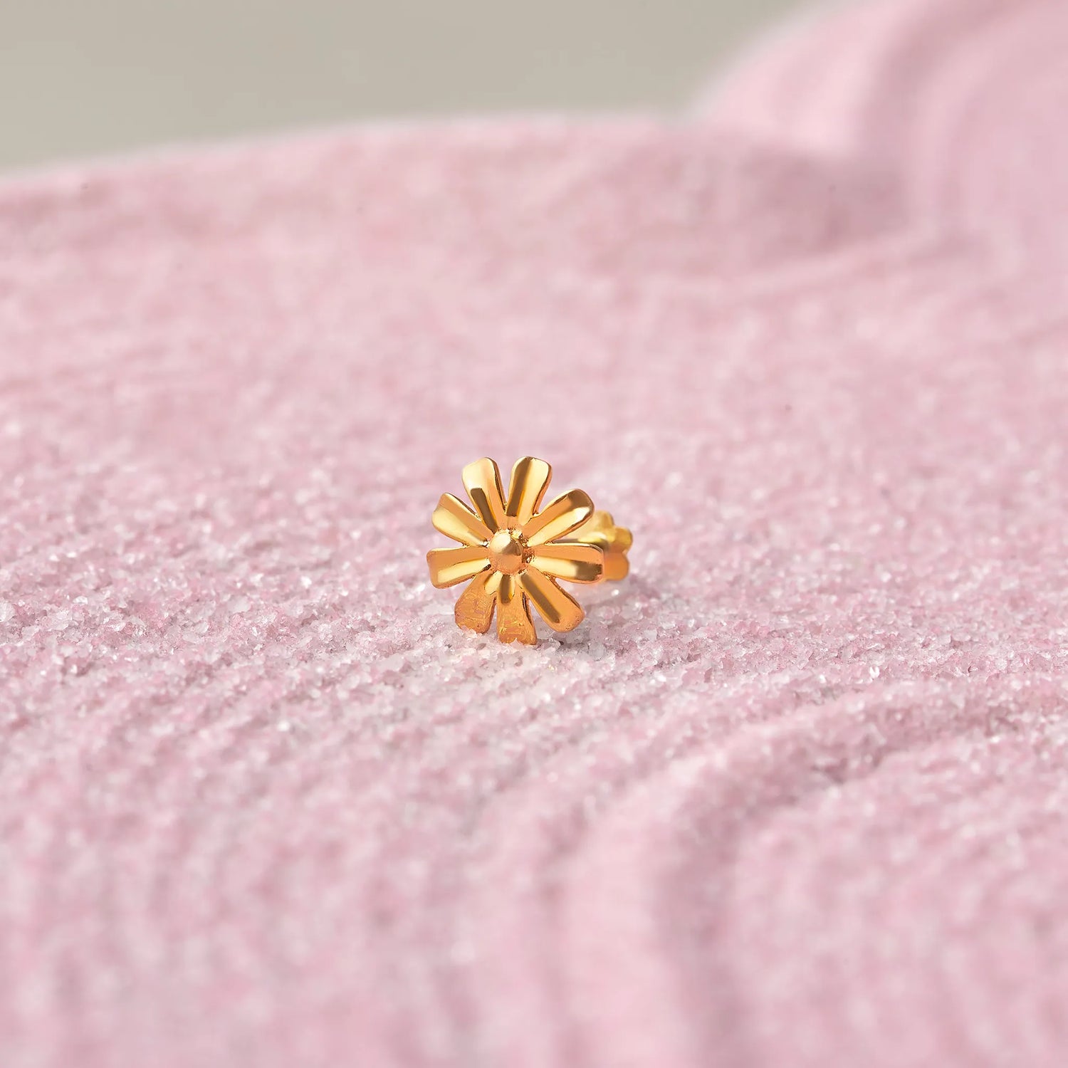 Close up of daisy flower inspired 18K gold nose pin placed on a soft pink textured fabric background