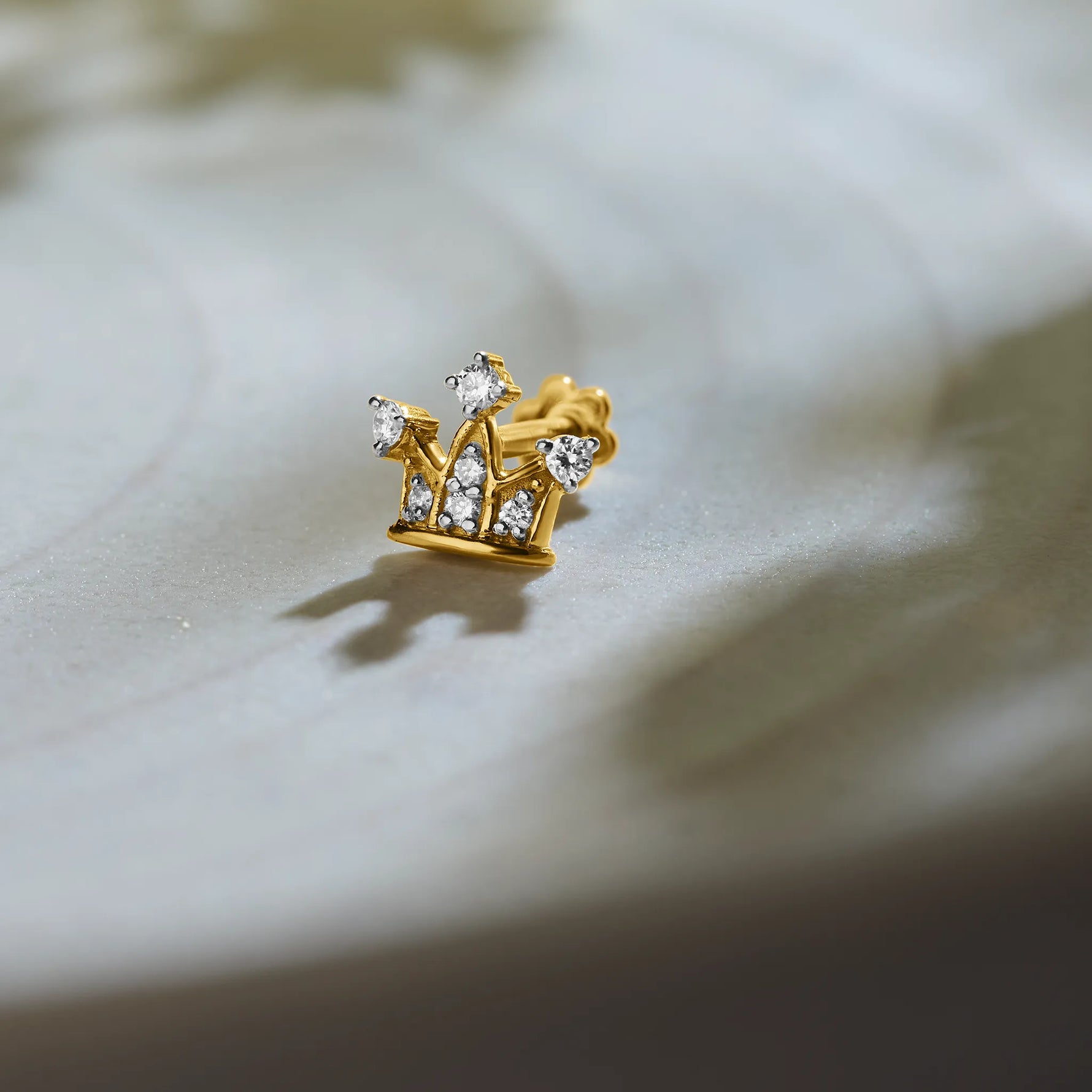 Trending gold nose pin with crown-inspired diamond design on textured background