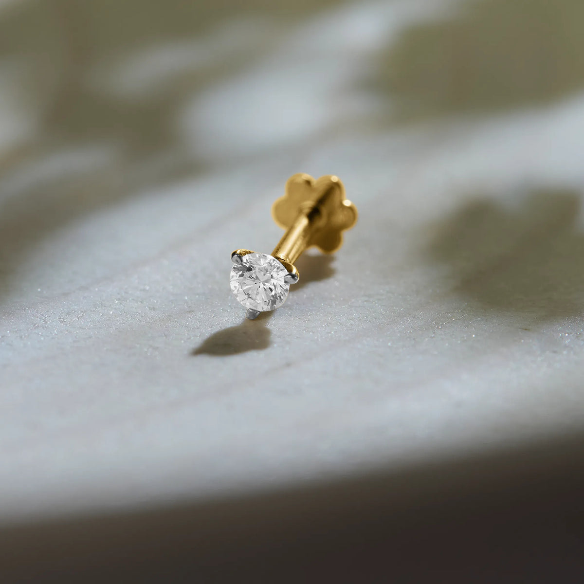 Diamond nose pin design from Kerala in gold with solitaire diamond on textured background