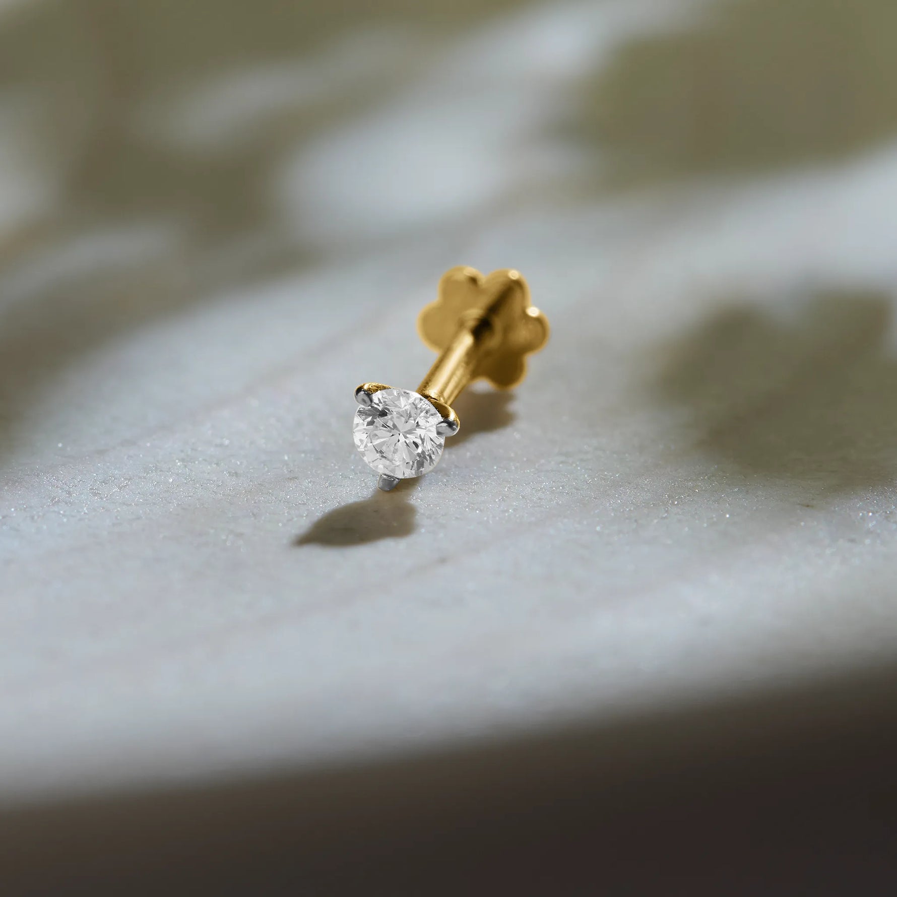 Diamond nose pin design from Kerala in gold with solitaire diamond on textured background
