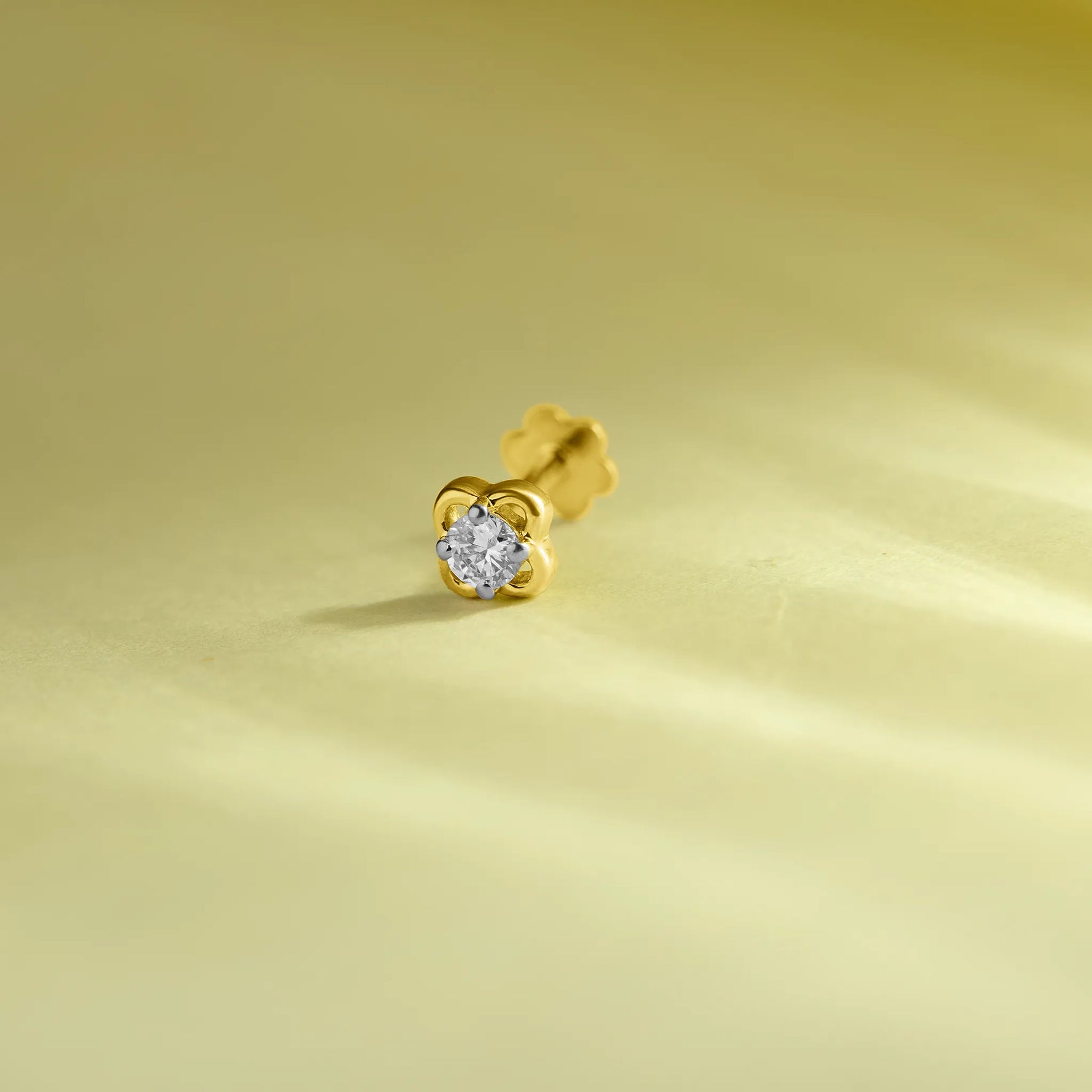Elegant gold flower nose pin with a sparkling round stone placed on a soft pastel green background.