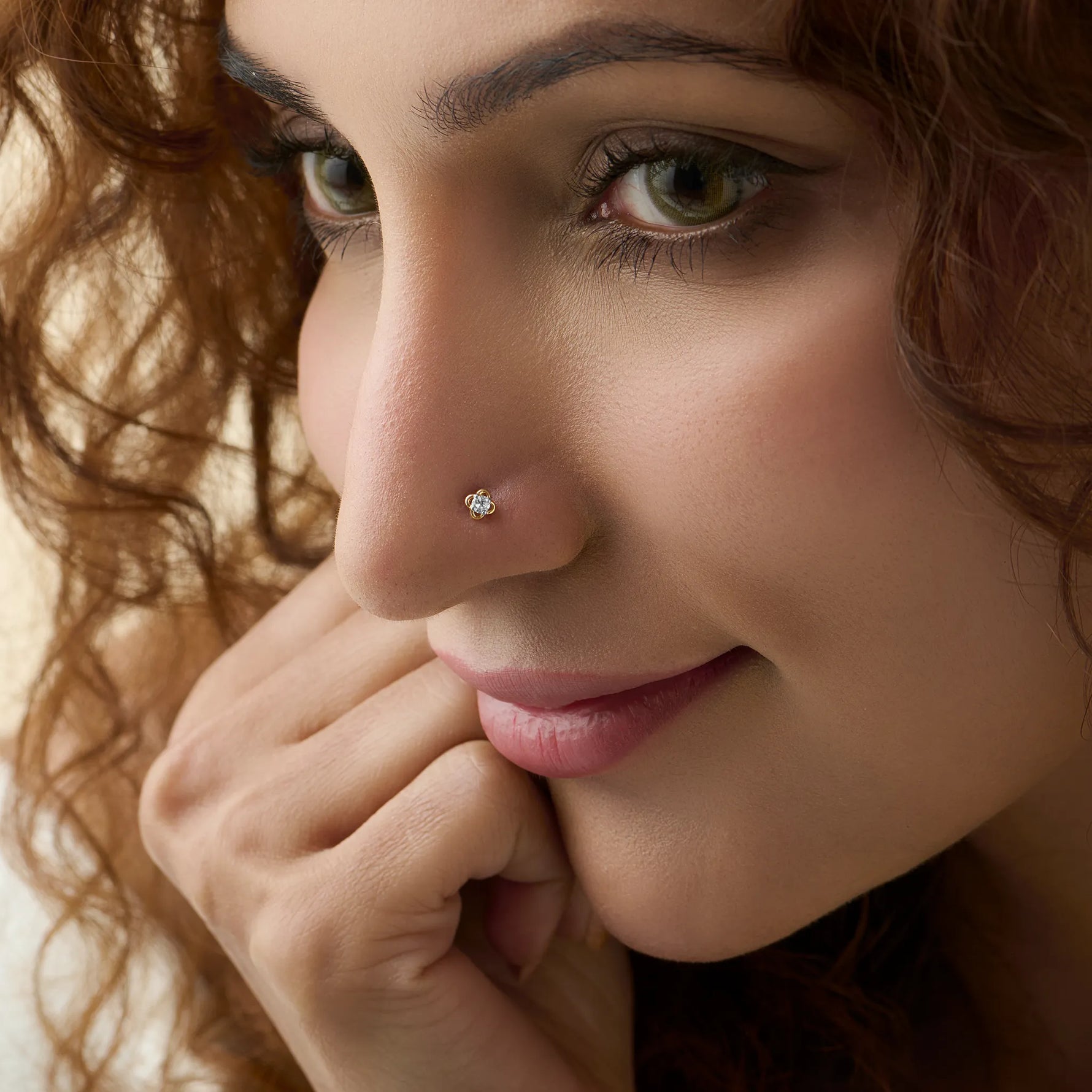 Close-up side profile of a woman wearing a delicate gold flower nose pin with a shiny stone.