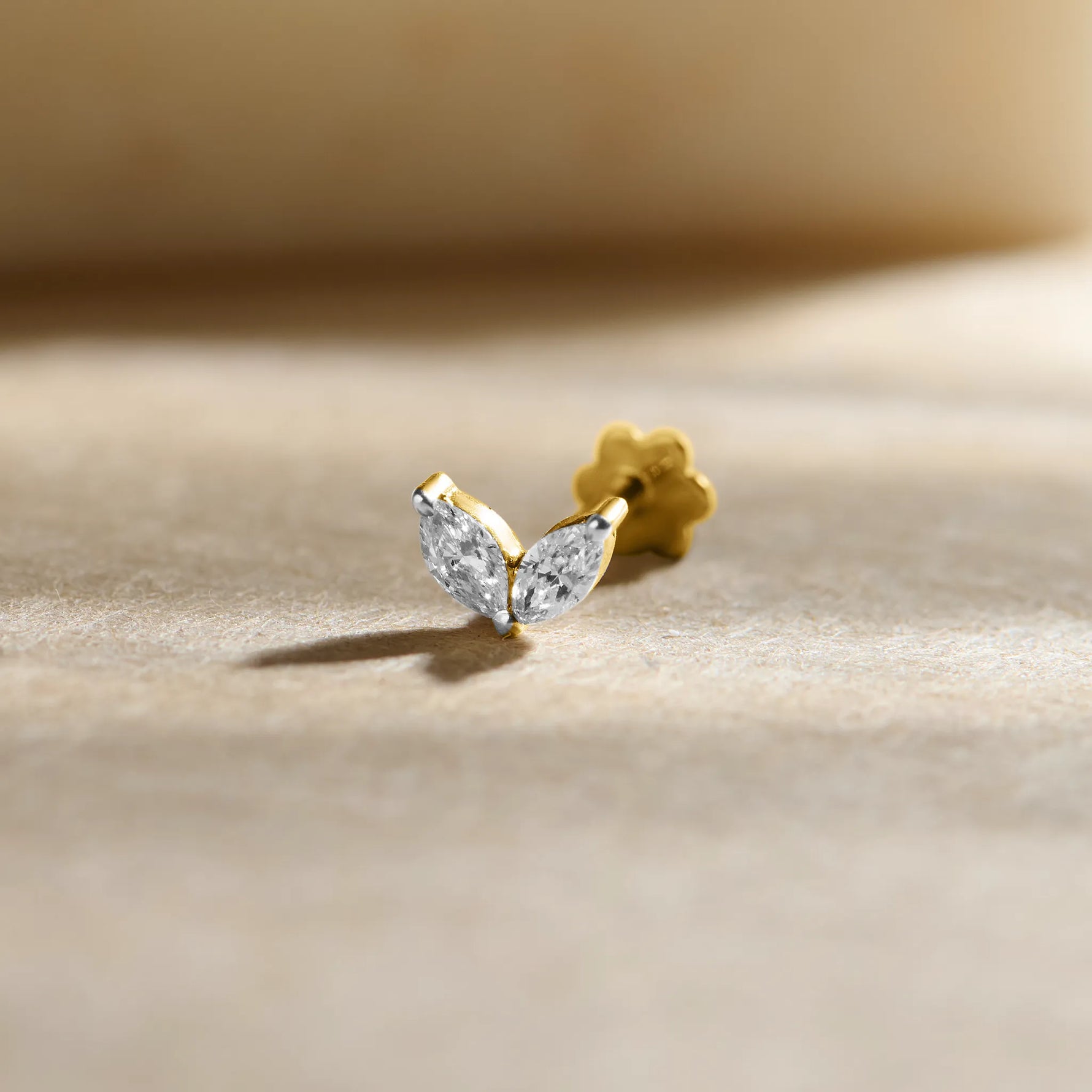 New nose pin design gold with elegant leaf-inspired twin stone pattern set in a polished gold base on a soft neutral background