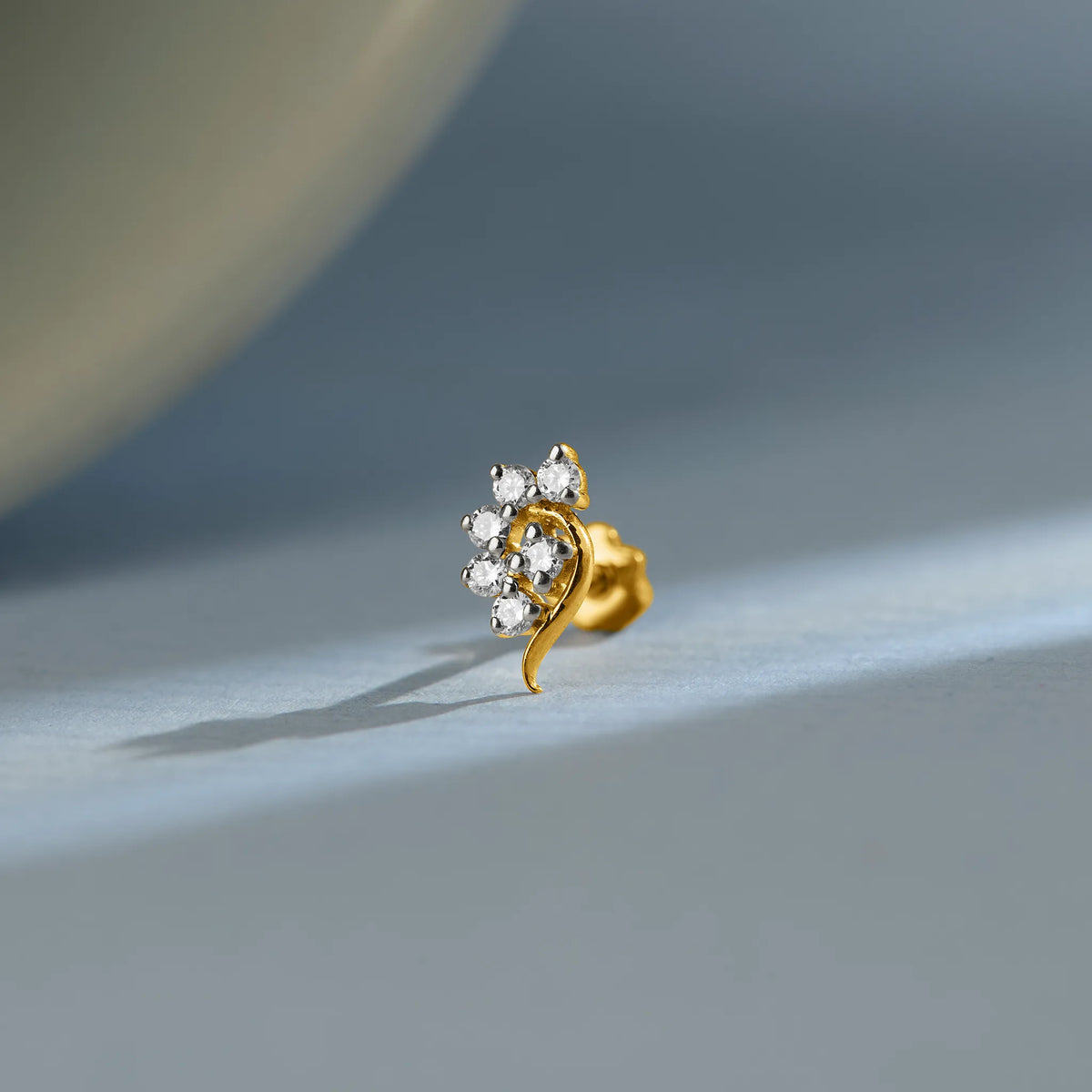 Curved floral gold nose pin design with sparkling diamonds on soft blue background