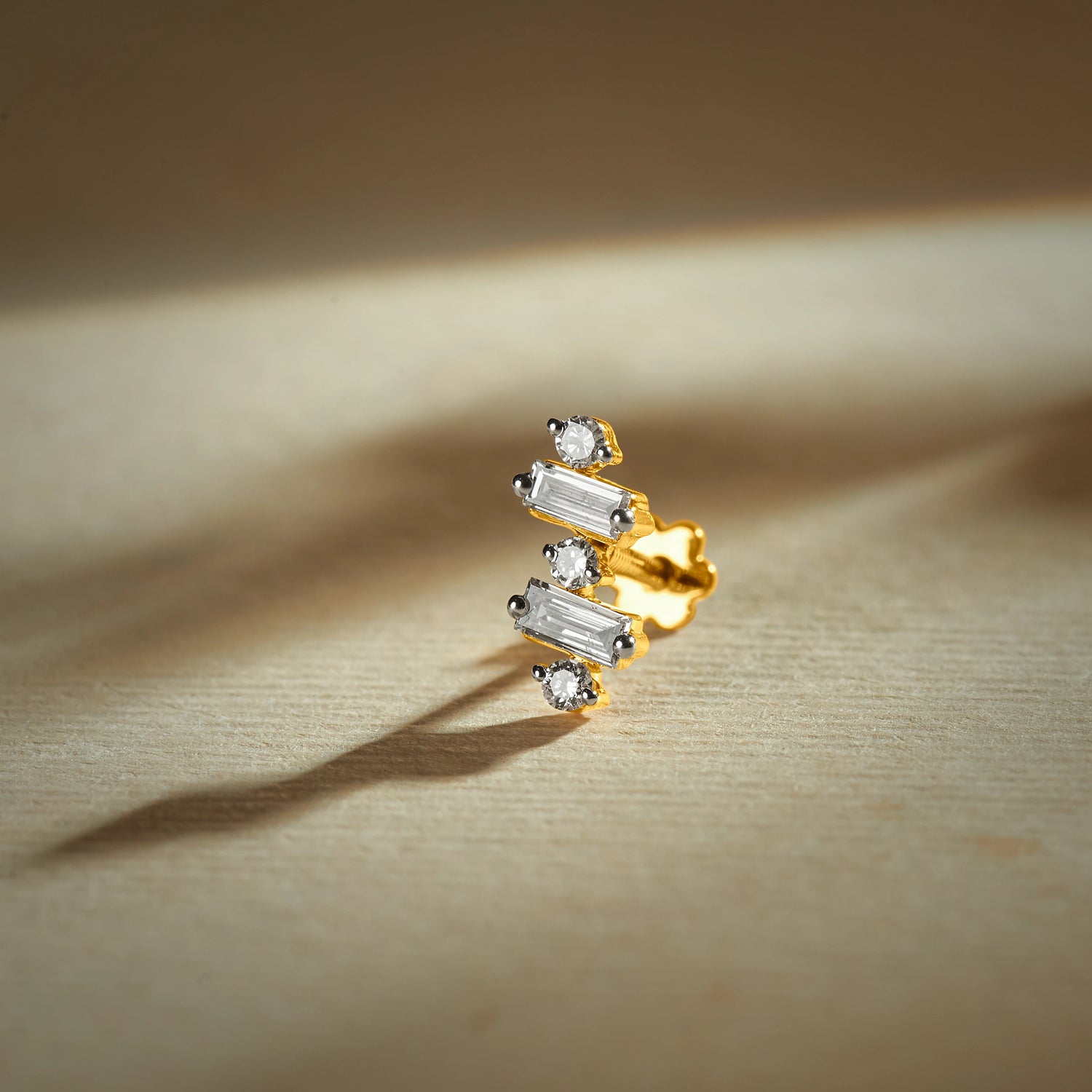 Nose pin gold with modern geometric design featuring baguette and round sparkling stones set in a polished gold base on a soft neutral background