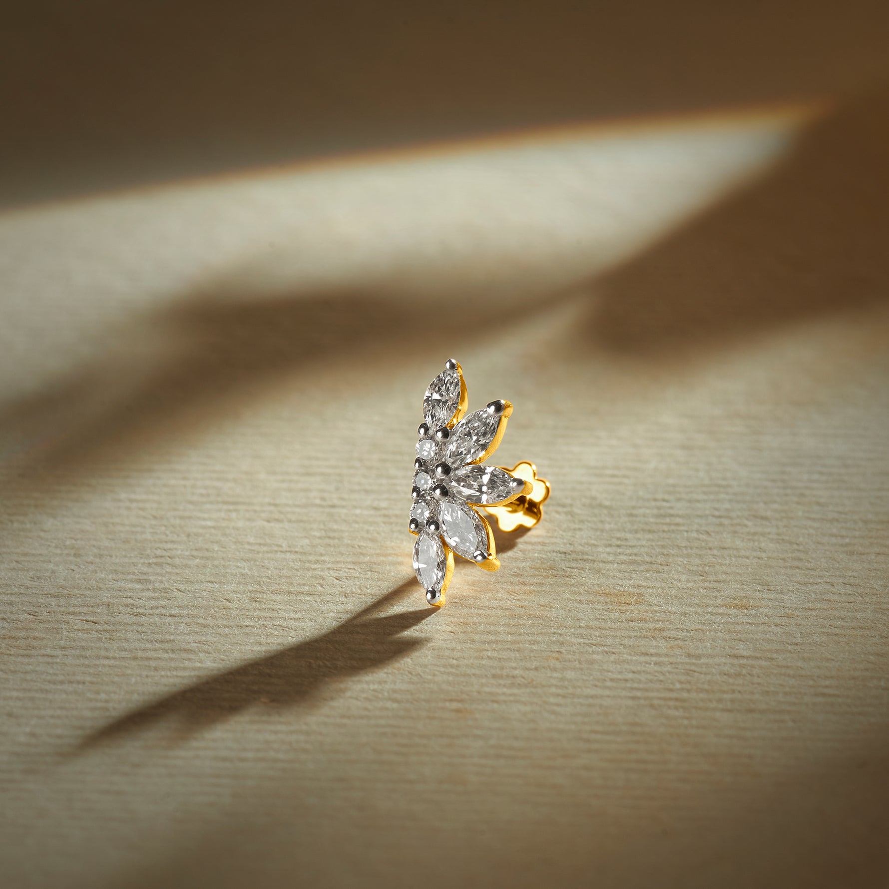 Flower nose pin gold with elongated floral leaf design featuring multiple sparkling stones set in a polished gold base on a soft neutral background