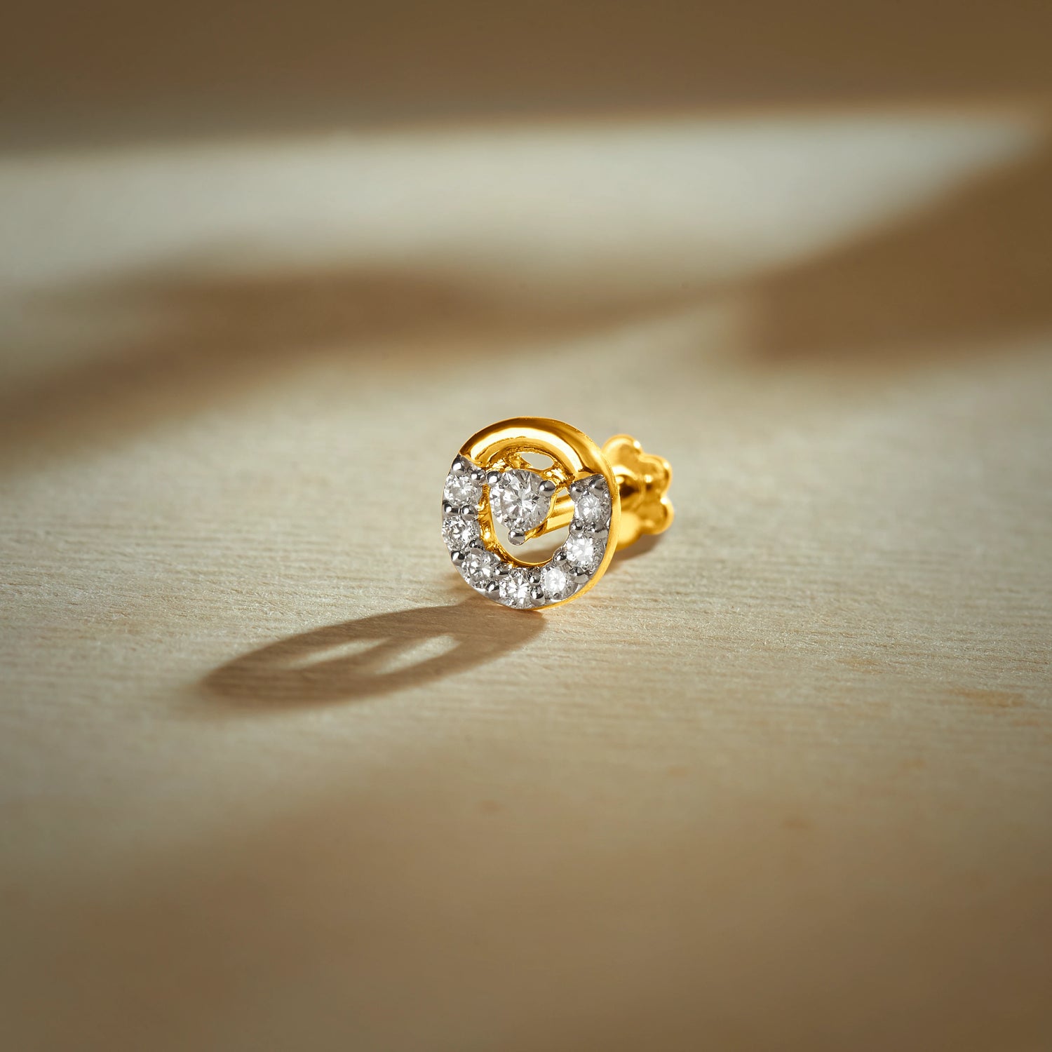 Gold nose pin with spiral circular design featuring sparkling stones set in a polished gold base on a soft neutral background