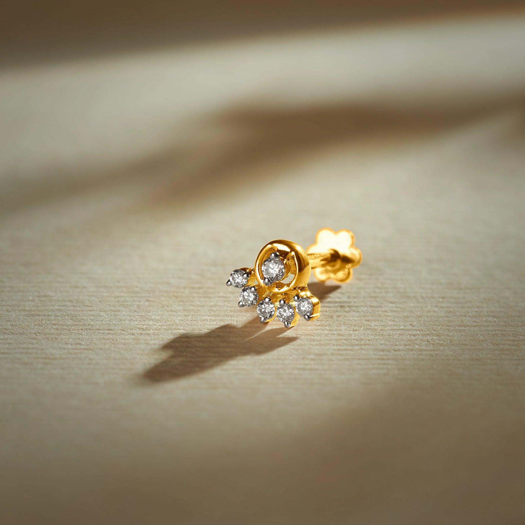 Gold nose pin with floral-inspired design featuring sparkling stones set in a polished gold base on a soft neutral background