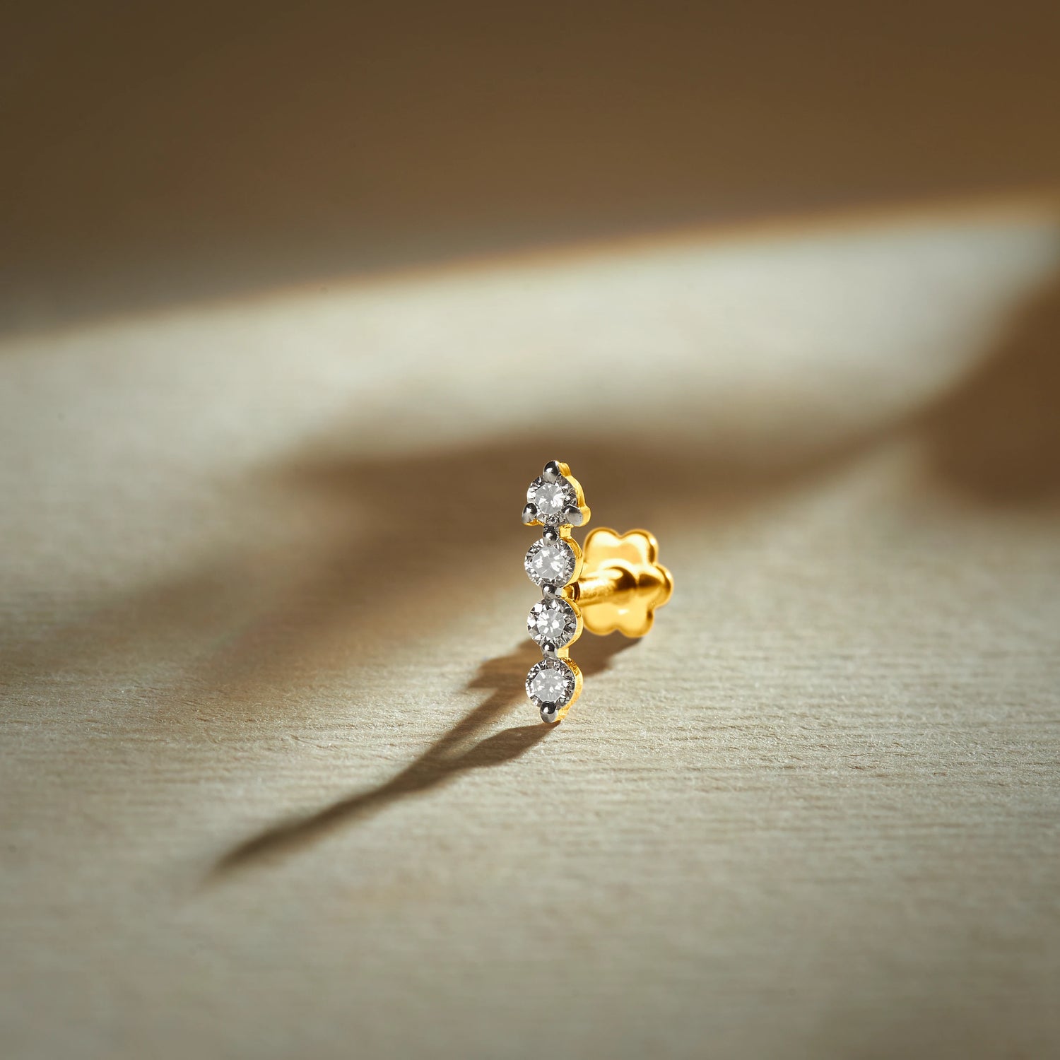 Gold nose pin with vertical row design featuring multiple sparkling stones set in a polished gold base on a soft neutral background