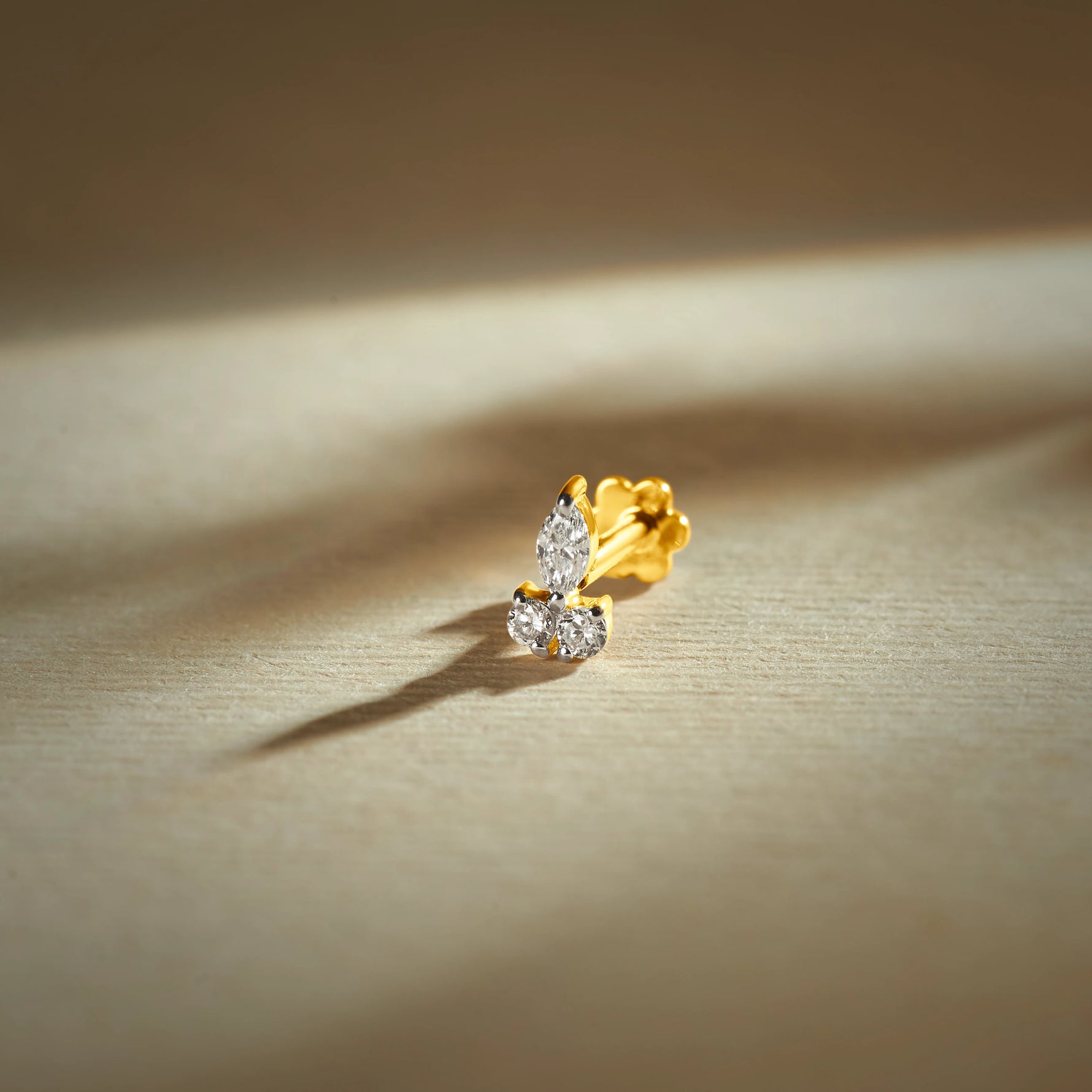 Gold nose pin with elegant curved design featuring two sparkling stones set in a polished gold base on a soft neutral background