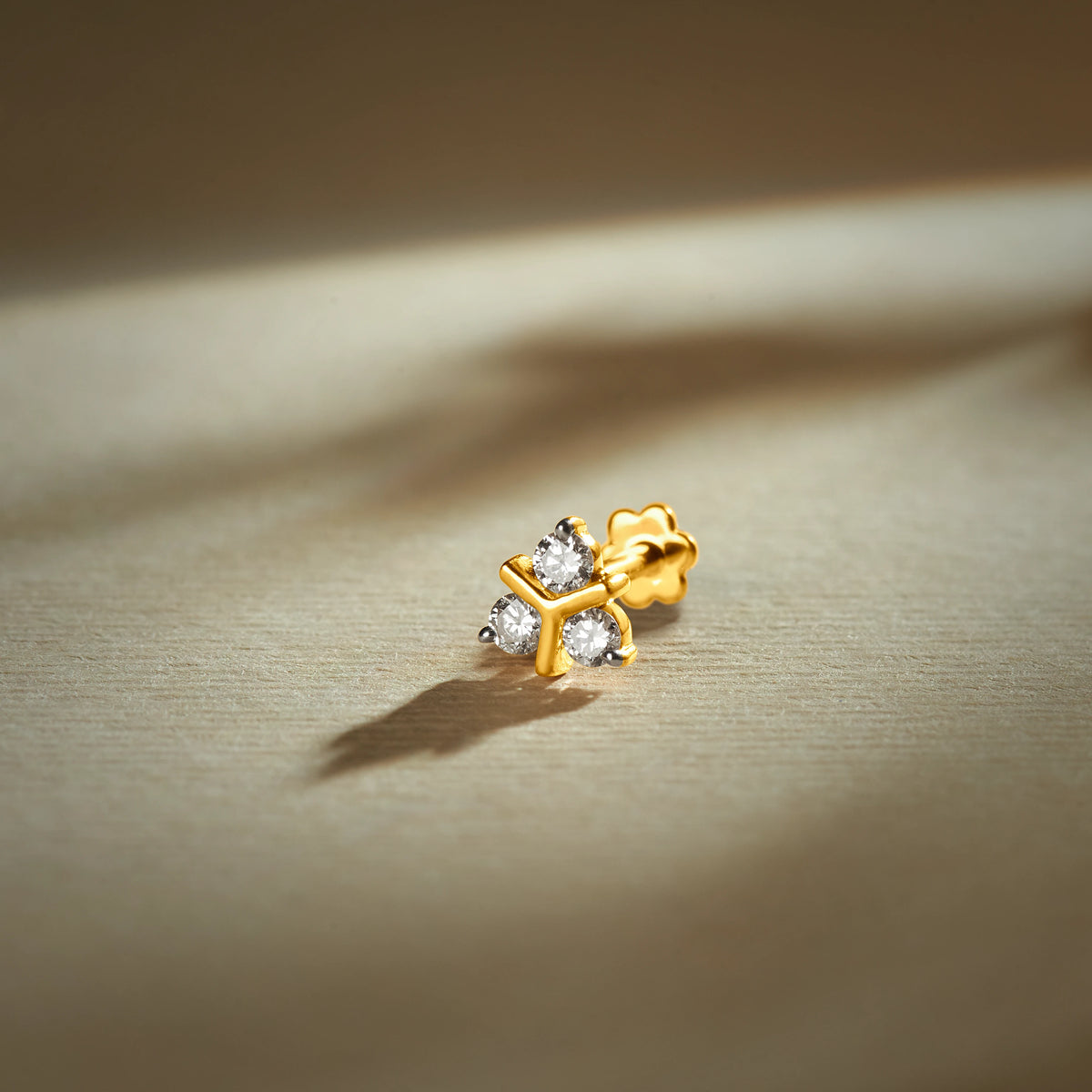 Nose pin gold with cross-style design featuring four sparkling stones set in a polished gold base on a soft neutral background