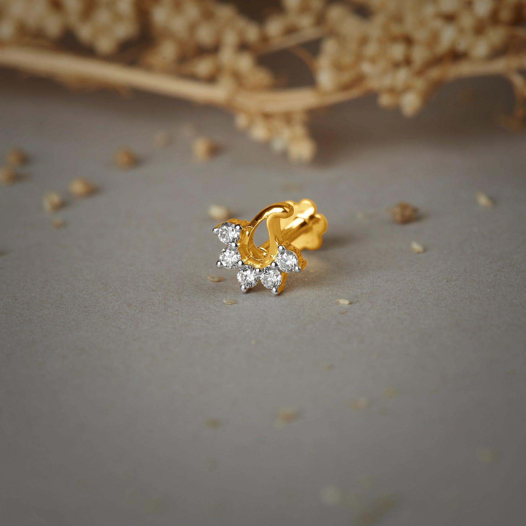 Nose pin gold with curved floral cluster design featuring sparkling stones set in a polished gold base on a soft neutral background