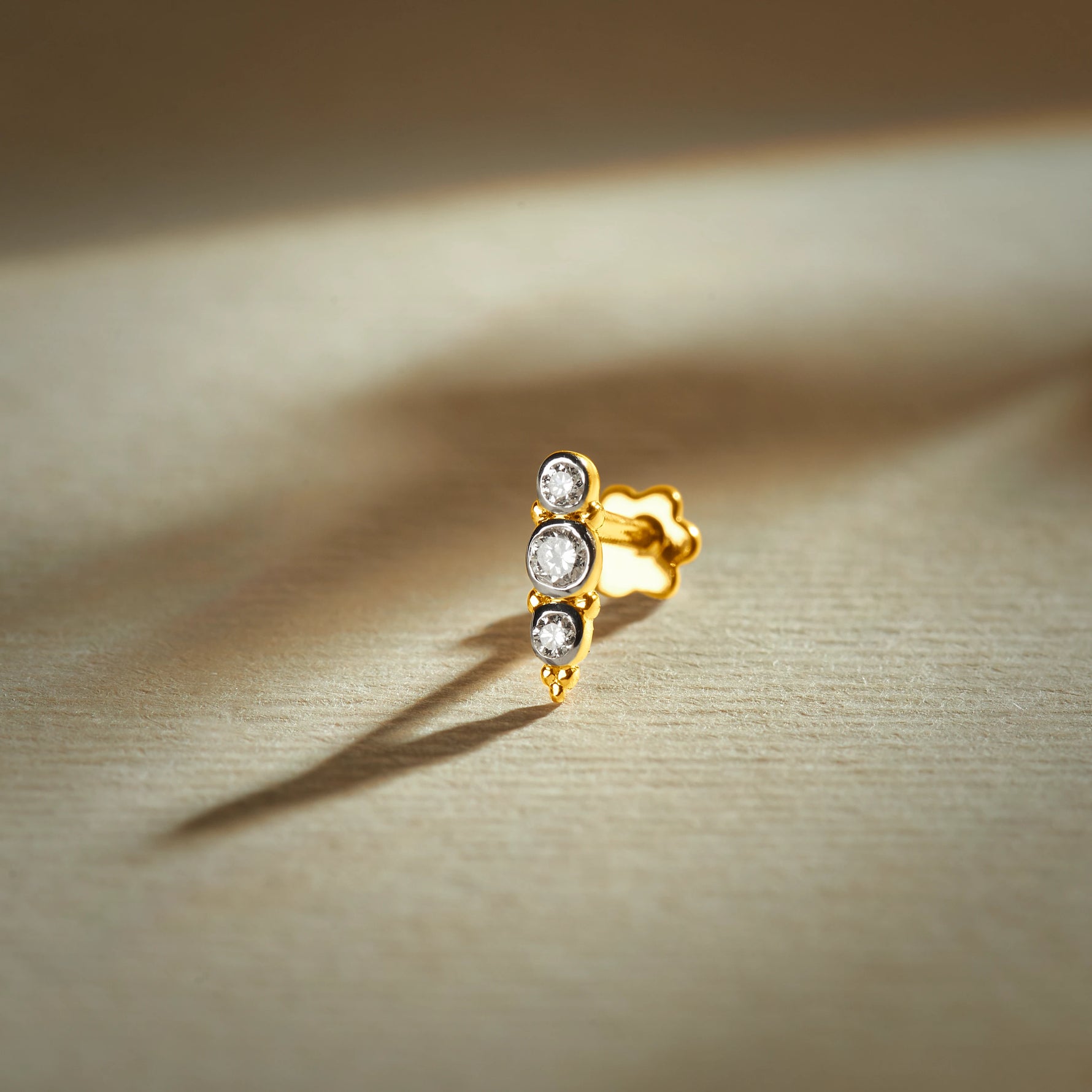 Nose pin gold with triple stone design featuring three sparkling stones set in a sleek gold base on a soft neutral background