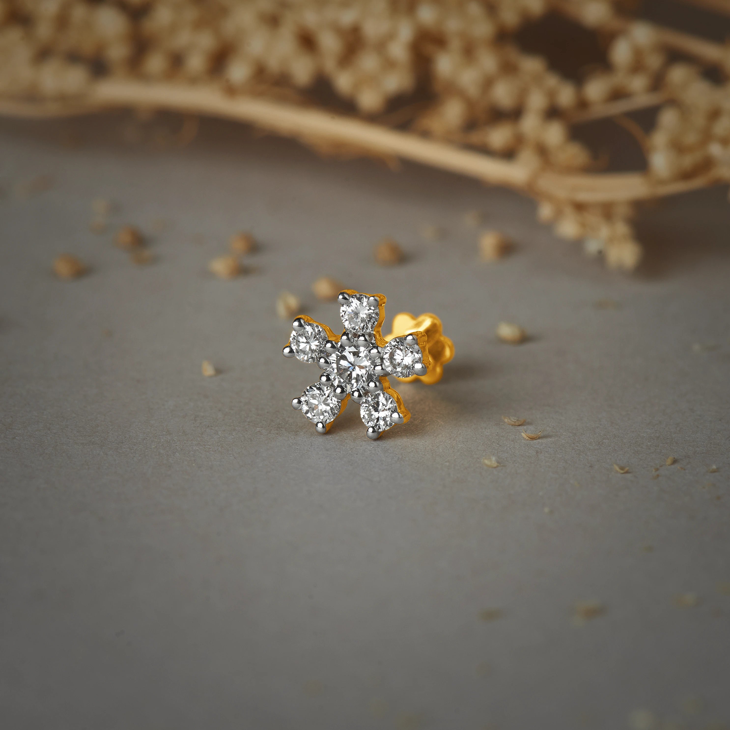 Nose pin gold with floral cluster design featuring sparkling stones set in a polished gold base on a soft neutral background