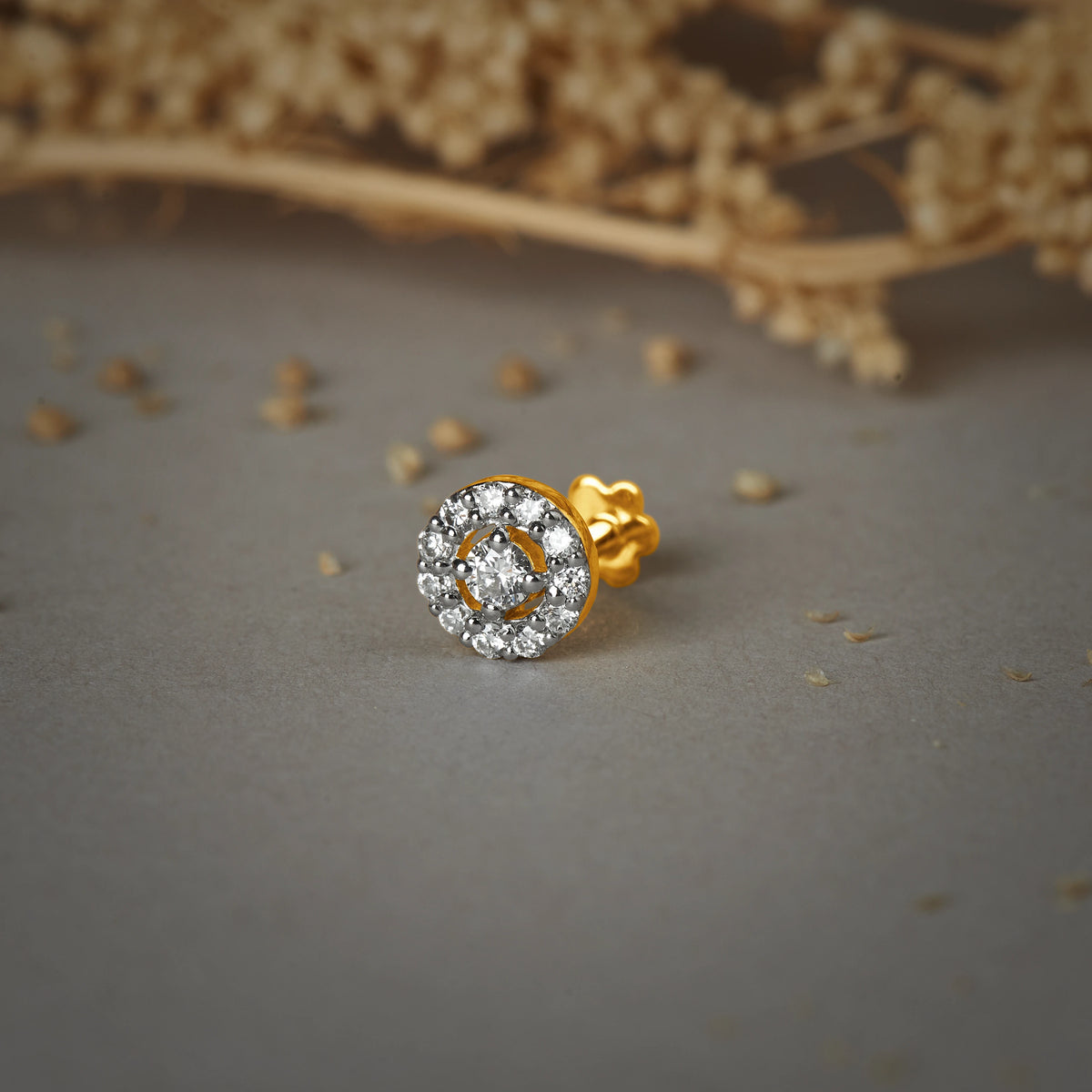 Nose pin gold with circular halo design featuring sparkling stones set in a polished gold base on a soft neutral background