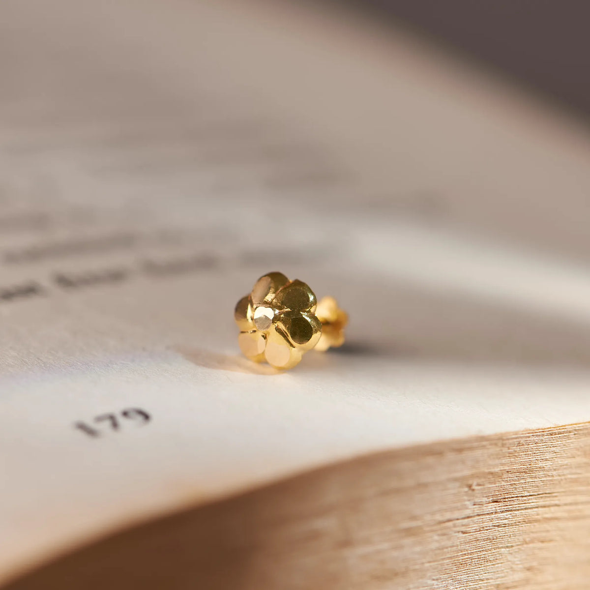 Close up of small flower inspired 18K gold nose pin placed on an open book page with soft natural lighting