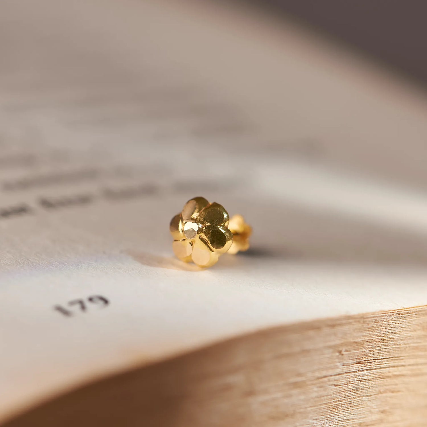 Close up of small flower inspired 18K gold nose pin placed on an open book page with soft natural lighting
