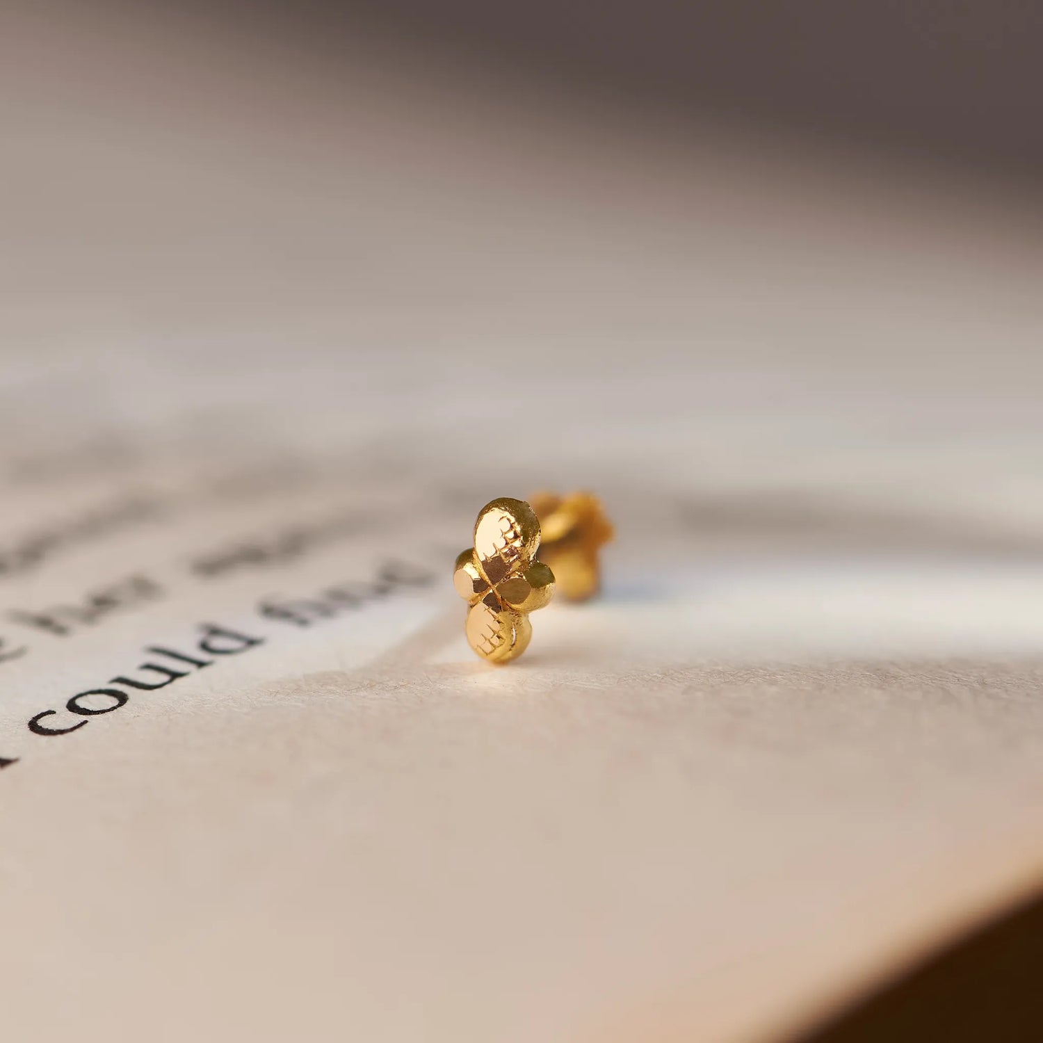 Close up of minimalist 18K gold nose pin placed on an open book page with soft natural lighting