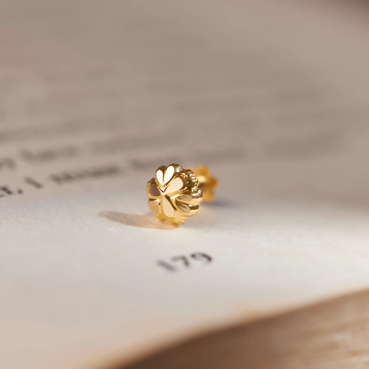 Close up of an 18K gold nose pin placed on an open book highlighting its intricate floral design and polished finish