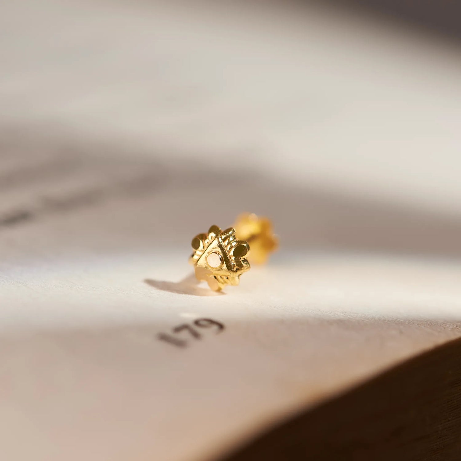 Close up of a small gold nose pin placed on an open book highlighting its intricate design and polished finish