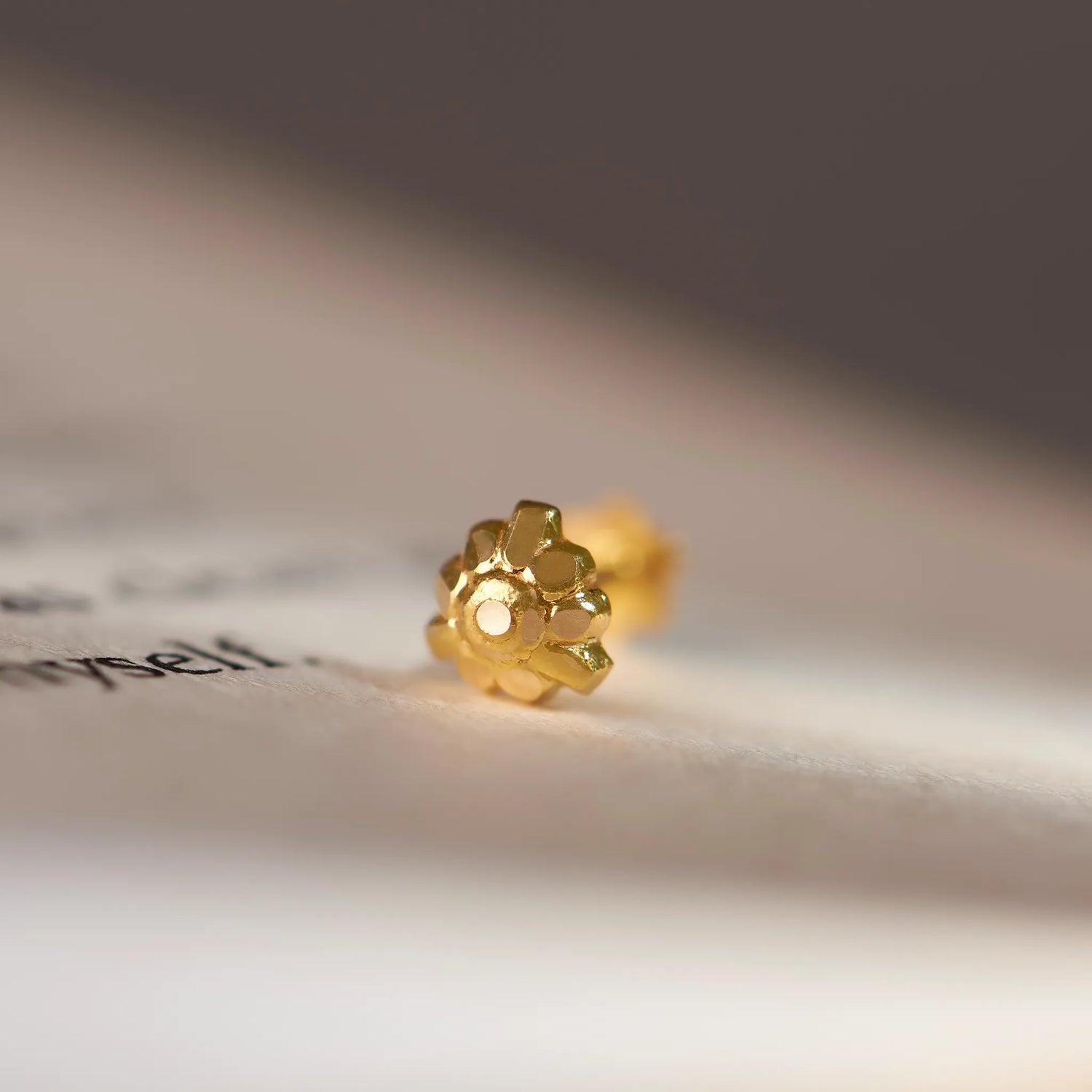 Close up of a floral gold nose pin placed on an open book page highlighting its intricate detailing and polished finish