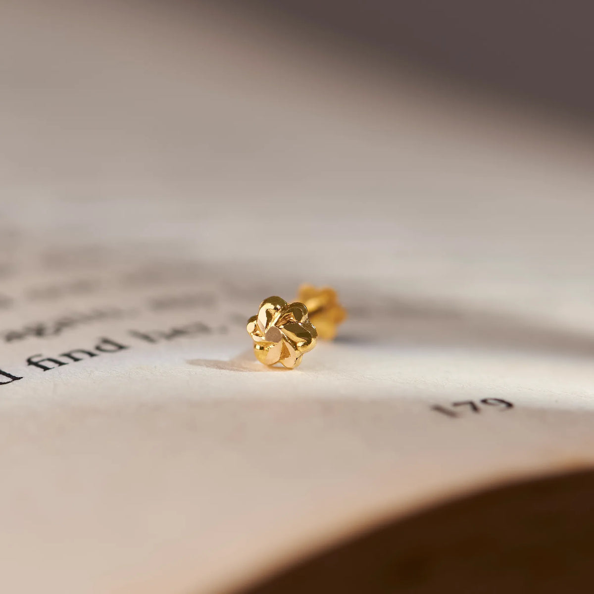 Close up view of a floral 18K gold nose pin placed on an open book page highlighting its intricate design and polished finish